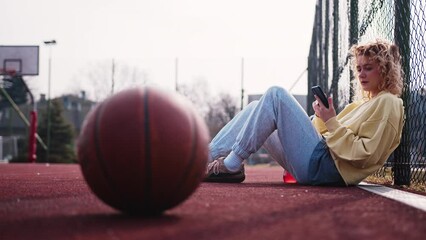 Young girl using smartphone while leaning on basketball field fence - Powered by Adobe