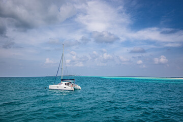 Fototapeta premium Beautiful turquoise water around white sailboat anchored in middle of ocean. Cloudy sky, ocean lagoon. Adventure travel, recreational seascape. Luxury activity, white yacht
