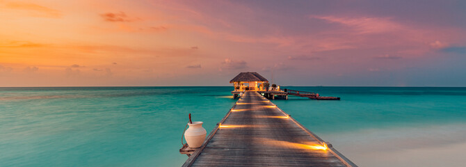 Amazing sunset island landscape at Maldives. Luxury resort water villas and jetty. Beautiful beach seascape with soft led lights colorful sky, background for vacation holiday. Paradise romance scenic