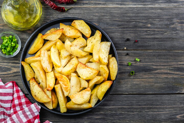 Seasoned potato wedges in cast iron skillet on wooden background. Top view, copy space, flat lay.