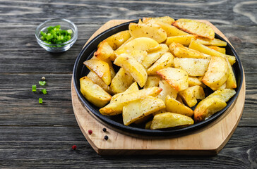 Baked garlic parmesan potato wedges in cast iron skillet on wooden background. Top view, copy space, flat lay.