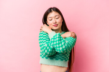 Young Chinese woman isolated on pink background hugs, smiling carefree and happy.