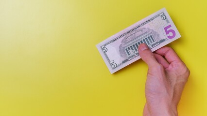 Man's hand is making a payment. Business Investment Economy Money Loan Saving Income Prosperity and Finance concept. Male hand showing dollar bills on yellow background. Five Dollar. 5 US Dollar.