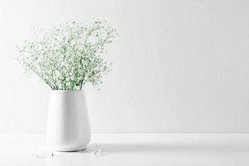 White floral background. Soft home decor, vase with white small flowers on  white background. 