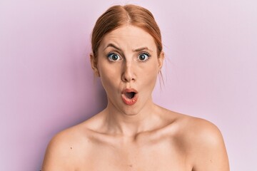 Young irish woman standing topless showing skin scared and amazed with open mouth for surprise,...