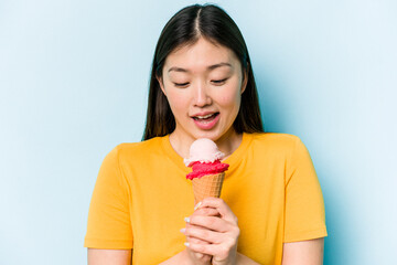 Young asian woman eating an ice cream isolated on blue background