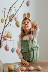Little girl decorating a tree with Easter eggs indoor