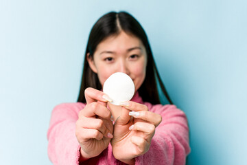 Young asian woman holding a facial disk isolated on pink background