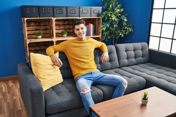 Young hispanic man smiling confident sitting on sofa at home