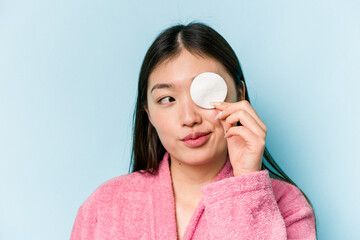 Young asian woman holding a facial disk isolated on pink background