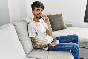 Young hispanic man using smartphone sitting on the sofa at home.
