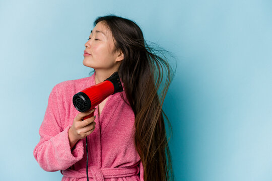 Young asian woman drying hair isolated on blue background