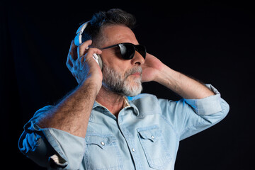 Enjoying his favorite music. Happy stylish man in hat and sunglasses with headphones listening and smiling while standing against blue neon background