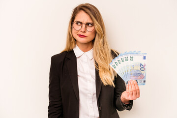 Young business caucasian woman holding a banknotes isolated on white background confused, feels doubtful and unsure.