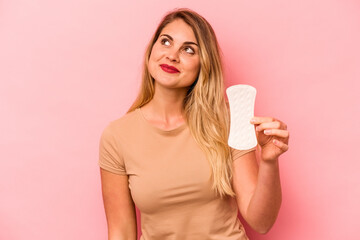 Young caucasian woman holding sanitary napkin isolated on pink background dreaming of achieving goals and purposes