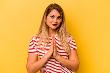 Young caucasian woman isolated on yellow background praying, showing devotion, religious person looking for divine inspiration.