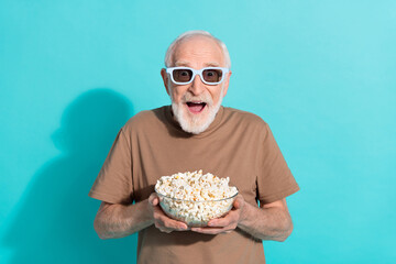 Portrait of attractive amazed cheerful grey-haired man eating popcorn having fun isolated over...