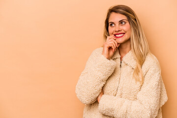 Young caucasian woman isolated on beige background relaxed thinking about something looking at a copy space.