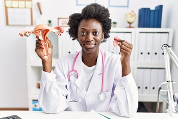 African doctor woman holding anatomical female genital organ and menstrual cup relaxed with serious...