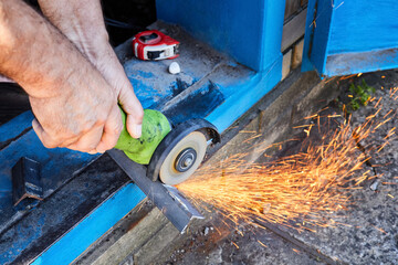 Cutting a metal corner with a circular saw with splashes of sparks. Garden work