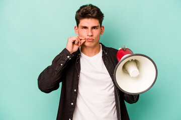 Young caucasian man holding a megaphone isolated on white background with fingers on lips keeping a...