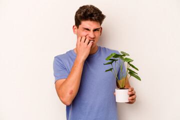 Young caucasian man holding a plant isolated on white background biting fingernails, nervous and very anxious.