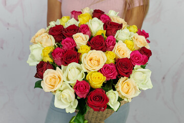a large bouquet of multicolored roses of red, white, pink, yellow, beige and green in the hands of a girl without a face on a light background