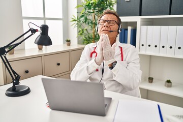 Senior doctor man working on online appointment begging and praying with hands together with hope expression on face very emotional and worried. begging.