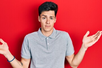 Young hispanic man wearing casual clothes clueless and confused with open arms, no idea and...