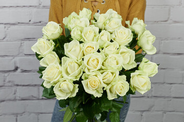 a bouquet of flowers made of white roses with blooming buds without packaging in the hands of a girl without a face on a light background