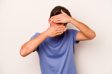 Young caucasian man isolated on white background blink at the camera through fingers, embarrassed covering face.