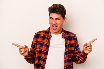 Young caucasian man isolated on white background pointing to different copy spaces, choosing one of them, showing with finger.