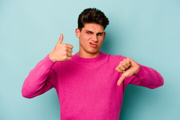 Young caucasian man isolated on blue background showing thumbs up and thumbs down, difficult choose...