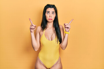 Young hispanic girl wearing swimsuit pointing up looking sad and upset, indicating direction with...