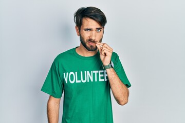 Young hispanic man wearing volunteer t shirt mouth and lips shut as zip with fingers. secret and...