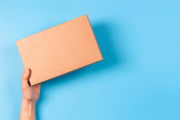 Top view to female hand holding brown cardboard box on light blue background. Mockup parcel box....