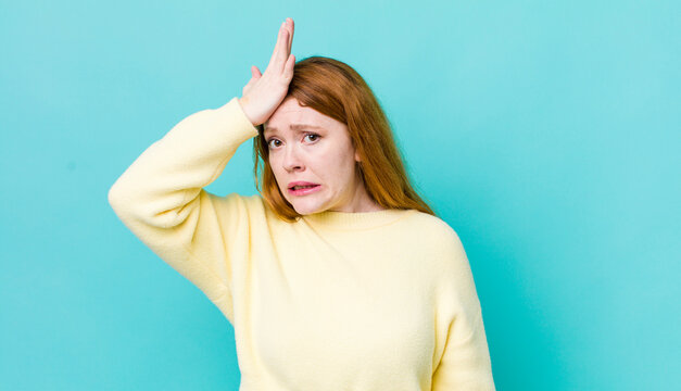 pretty red head woman raising palm to forehead thinking oops, after making a stupid mistake or remembering, feeling dumb