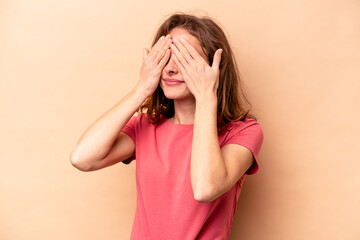 Young caucasian woman isolated on beige background afraid covering eyes with hands.