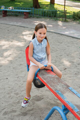 Fototapeta na wymiar smiling girl in shorts riding seesaw in summer park.