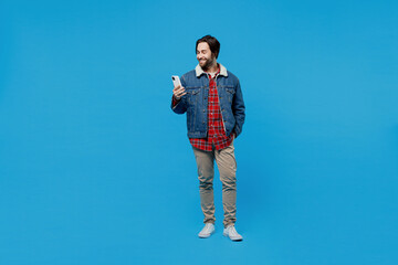 Full size body length young brunet bearded man 20s wear warm denim jacket hold in hand use mobile...
