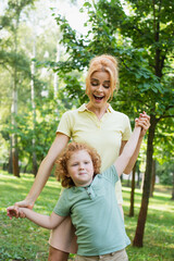 excited woman holding hands of son while having fun in summer park.