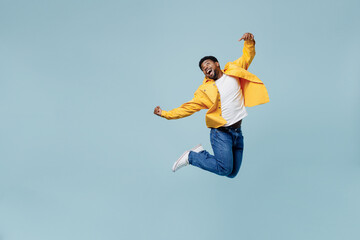 Full body young man of African American ethnicity 20s in yellow shirt jump high clench fist do winner gesture isolated on plain pastel light blue background studio portrait. People lifestyle concept