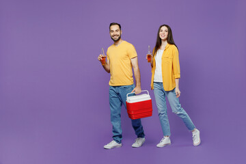 Full size young couple two friends family man woman together wear yellow clothes hold red box freezer cooler refrigerator bottle drink beer walk go isolated on plain violet background studio portrait.