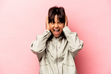 Young hispanic woman isolated on pink background covering ears with hands trying not to hear too loud sound.