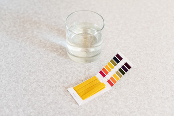 Glass of water, quality tester and universal litmus ph tester with color scale. Measuring the...