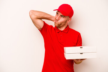 Young delivery caucasian man holding pizzas isolated on white background touching back of head, thinking and making a choice.