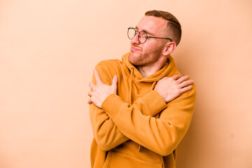 Young caucasian man isolated on beige background hugs, smiling carefree and happy.