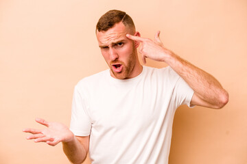 Young caucasian man isolated on beige background showing a disappointment gesture with forefinger.