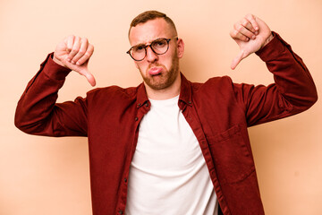 Young caucasian man isolated on beige background showing a dislike gesture, thumbs down....