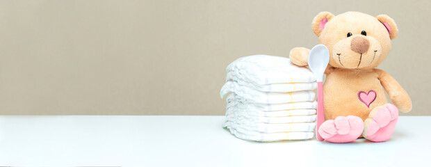 Stack of diapers with toy teddy bear with spoon on table. set for baby shower with copy space